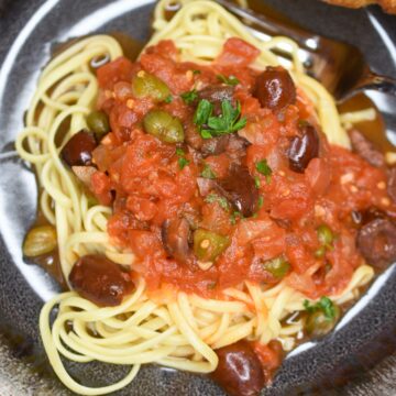 Puttanesca Sauce overtop pasta in bowl.