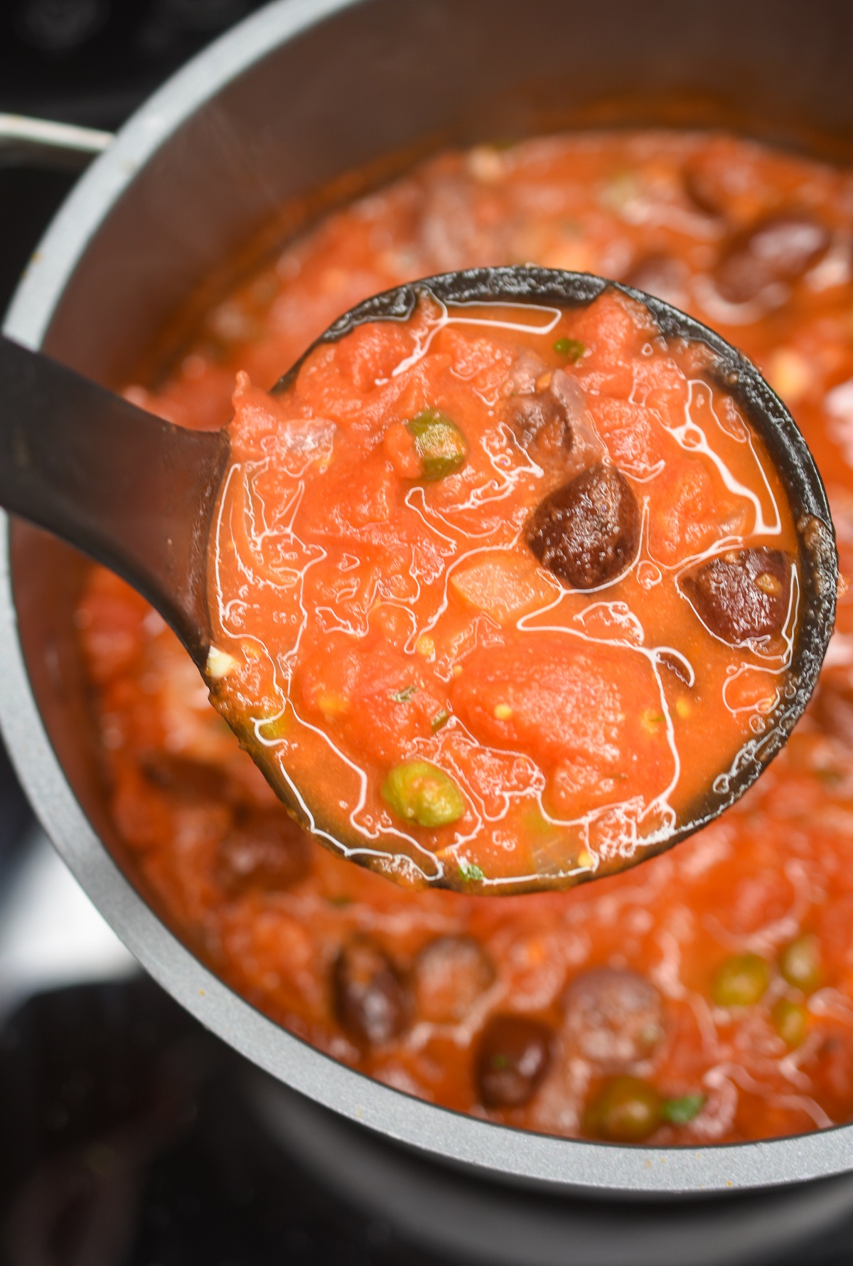 Pot of Puttanseca Sauce on stove with a ladle holding the homemade sauce.