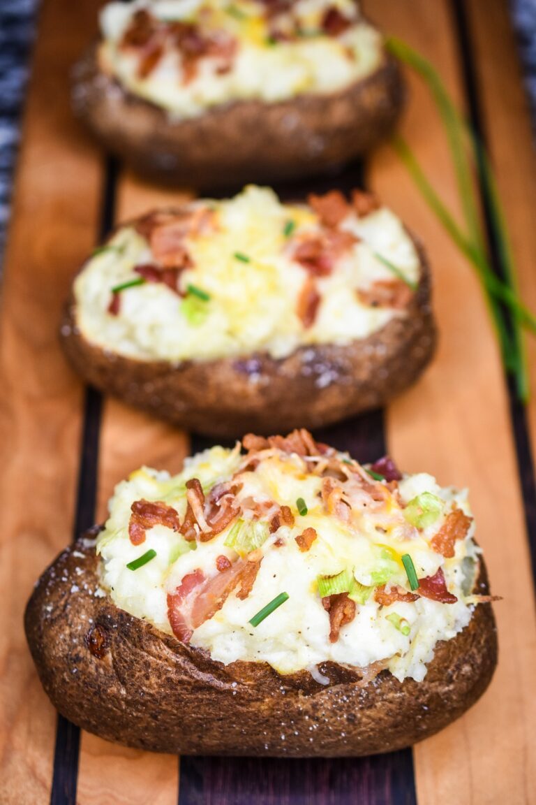 How to make Twice Baked Potatoes. Shown 3 twice baked potatoes topped with bacon cheese and chives on a wood board