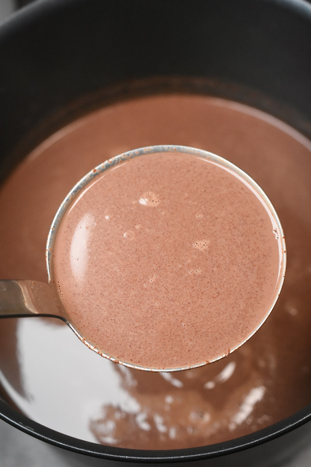 Large pot full of hot cocoa, a metal ladle scooping some out of mot.