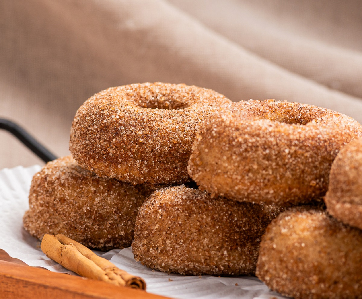 Pile of Apple Cider Donuts on a parchment paper lined wooden tray rolled in Spiced Sugar