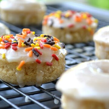 Baked Apple Cider Donuts on a baking rack. Dipped in Apple Cider glaze, some garnished with fall colored sprinkles