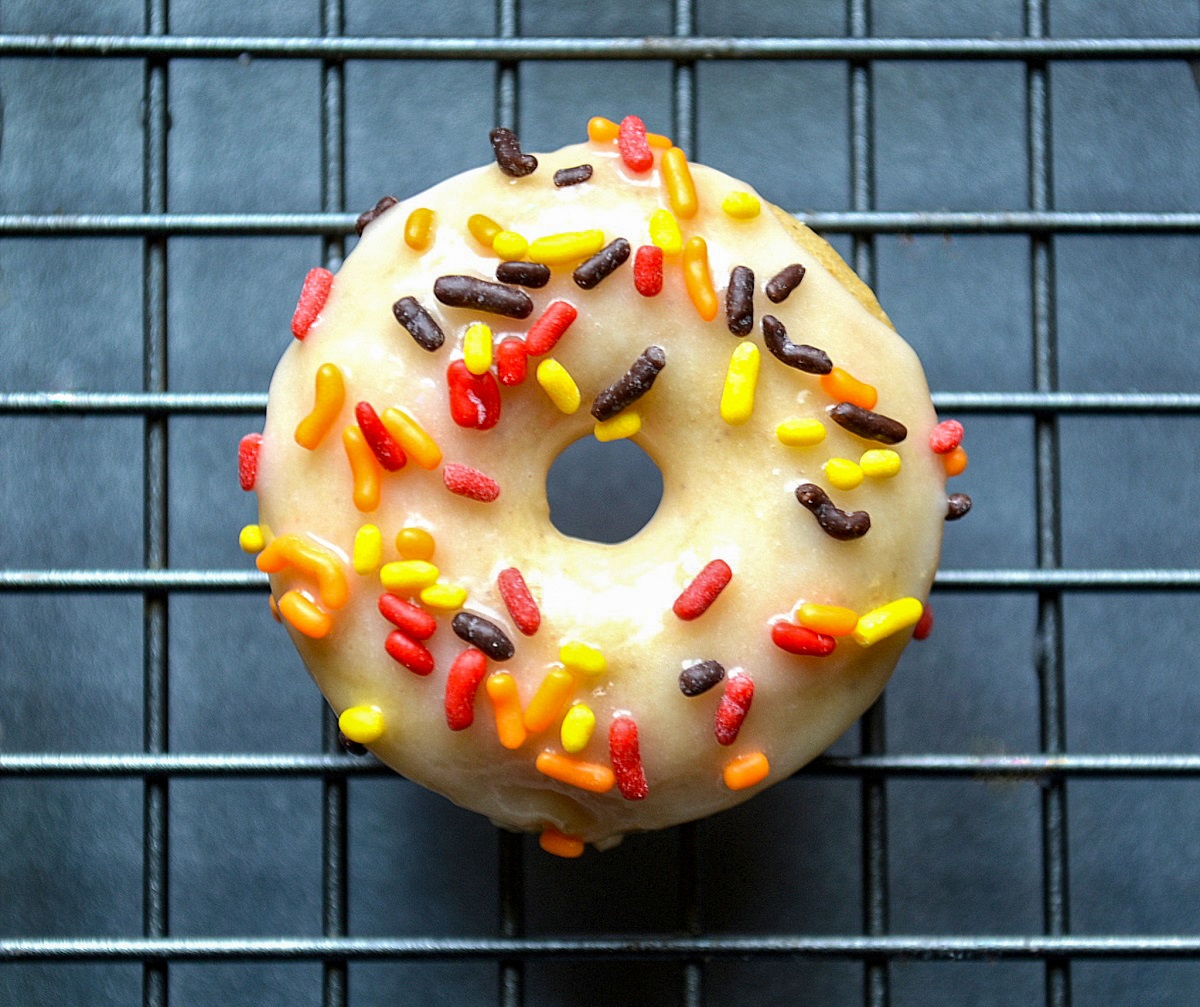 single apple cider donut dipped in apple cider glaze speckl;ed with fall colored sprinkles on a wire rack