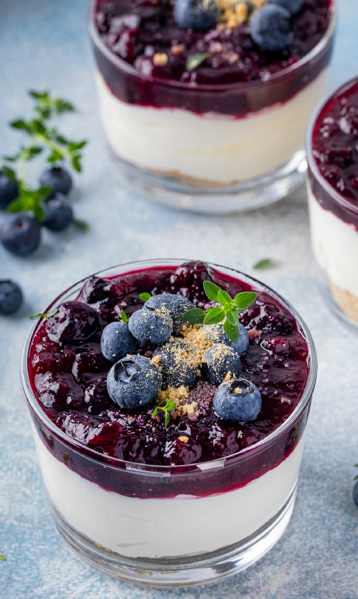 These tasty cheesecake parfaits are easy to make! Blueberry Cheesecake Shooters make a fabulous party dessert. Topped with Blueberry Compote, this easy party dessert is delicious! Shown in small glass ramekins. Fresh blueberries garnishing the dessert. Graham cracker crumb base, no bake cheesecake filling and blueberry compote.