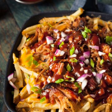 CAst iron skillet filled with French fries topped with pulled pork with BBQ sauce drizzle, scallions and red onion