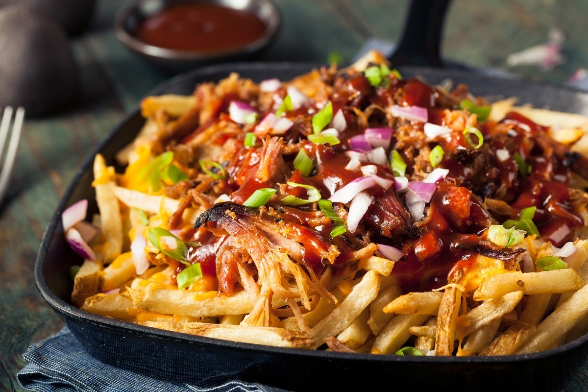 Cast iron pan with French fries topped with pulled pork. Garnished with barbecue sauce, scallions and red onions.