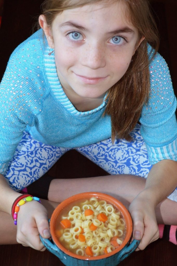 Young girl holding bowl of chicken noodle soup