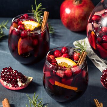 Winter Sangria recipe is a great holiday drink recipe and food gift too. Also called Christmas Sangria, this is tasty all winter long! SHown in 2 glasses garnished with cranberries, satsumas rosemary sprigs and cinnamon stics.