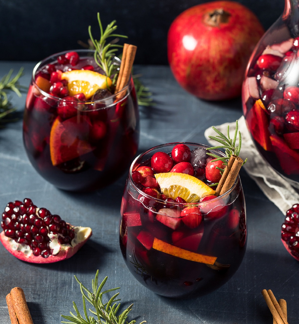 Winter Sangria recipe, shown in 2 glasses filled with red sangria also called Christmas Sangria. Garnished with satsumas, rosemary, pomegranates and cranberries.