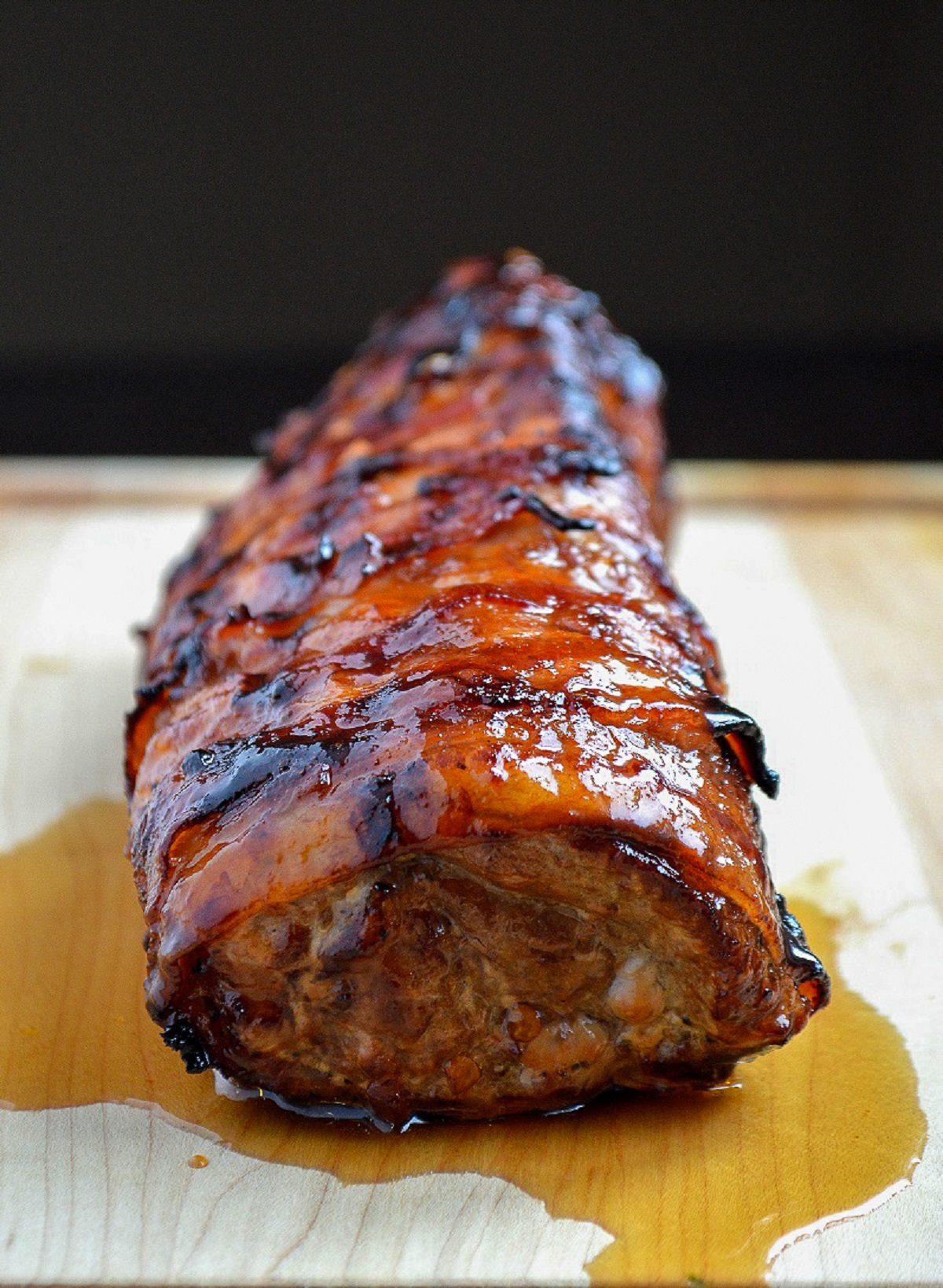 Grilled Bacon Wrapped Pork Tenderloin on a wood board with honey chipotle sauce.