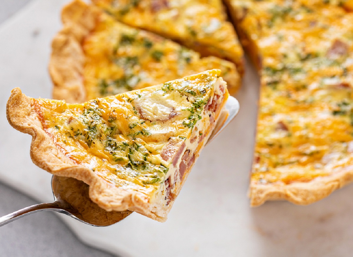 Breakfast Pie shown partially sliced with one slice held by a metal pie server. Broccoli, cheese and egg pie.