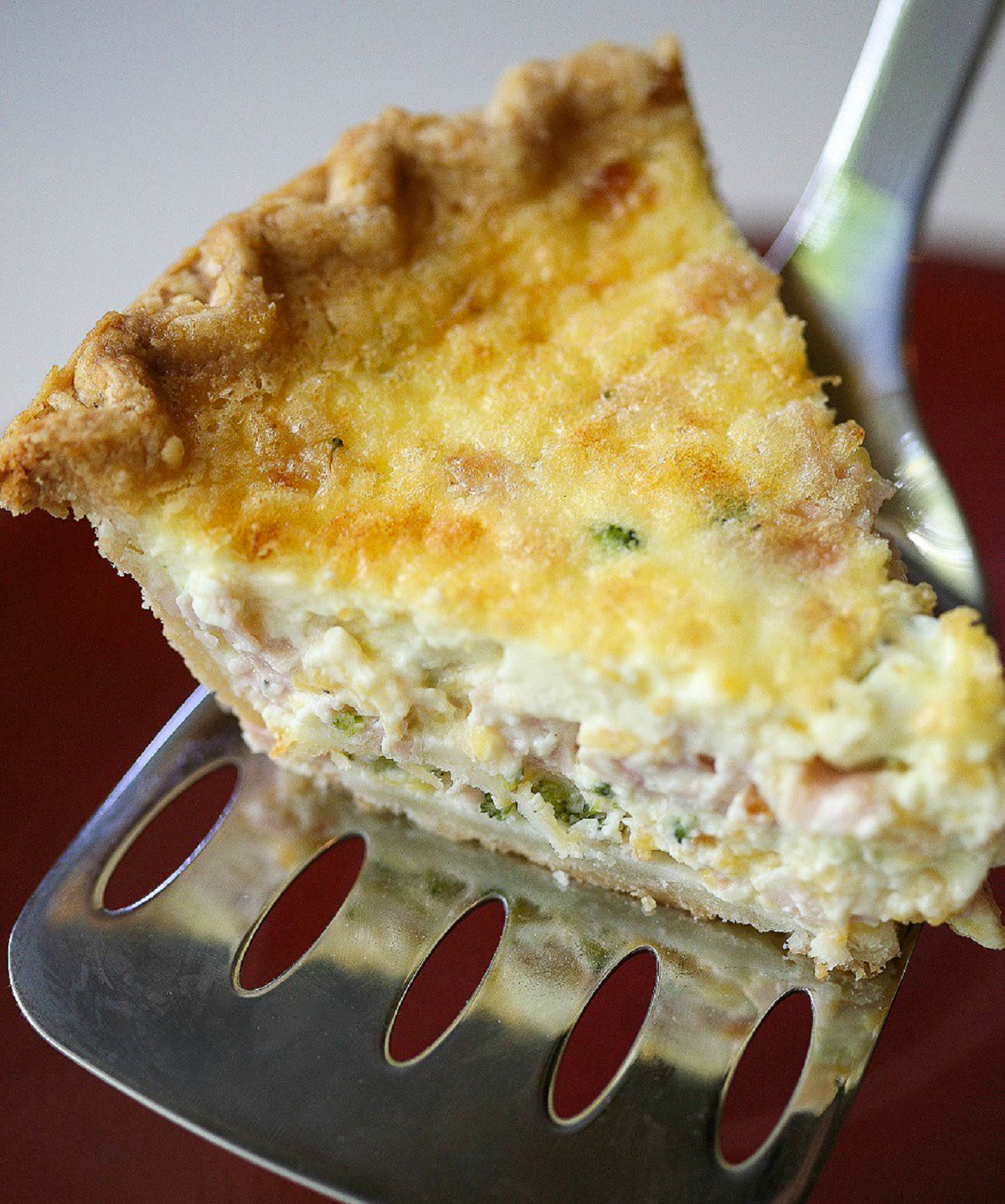 Breakfast Pie made with eggs, ham, cheese and broccoli shown baked with one slice on a metal spatula.