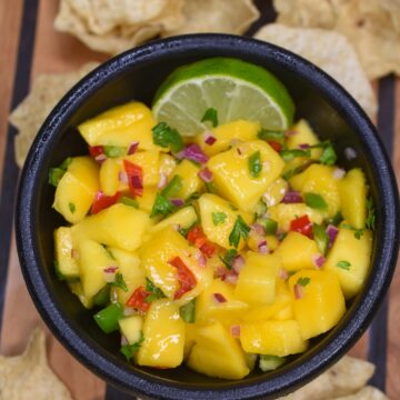 Mango Salsa Recipe shown in black bowl with lime wedge accompanied by tortilla chips