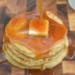 Apple Cider Pancakes with Apple Cider Syrup shown as a stack of 4 pancakes with a pat of butter on top with apple cider syrup being drizzled onto pancakes.