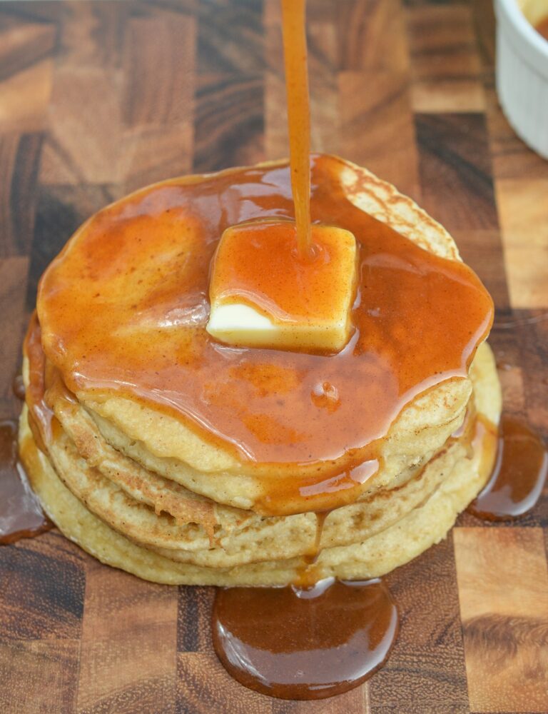 Apple Cider Pancakes with Apple Cider Syrup shown as a stack of 4 pancakes with a pat of butter on top with apple cider syrup being drizzled onto pancakes.