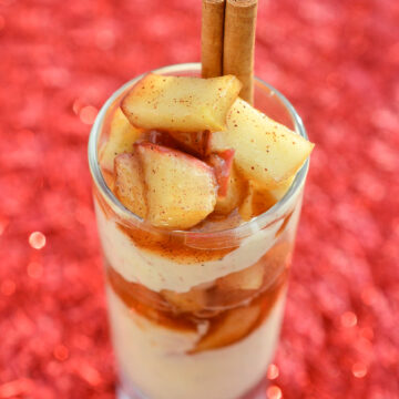 Apple Pie Cheesecake Shooter in a mini dessert glass. Layed no bake cheesecake and fried apples garnished with a cinnamon stick.