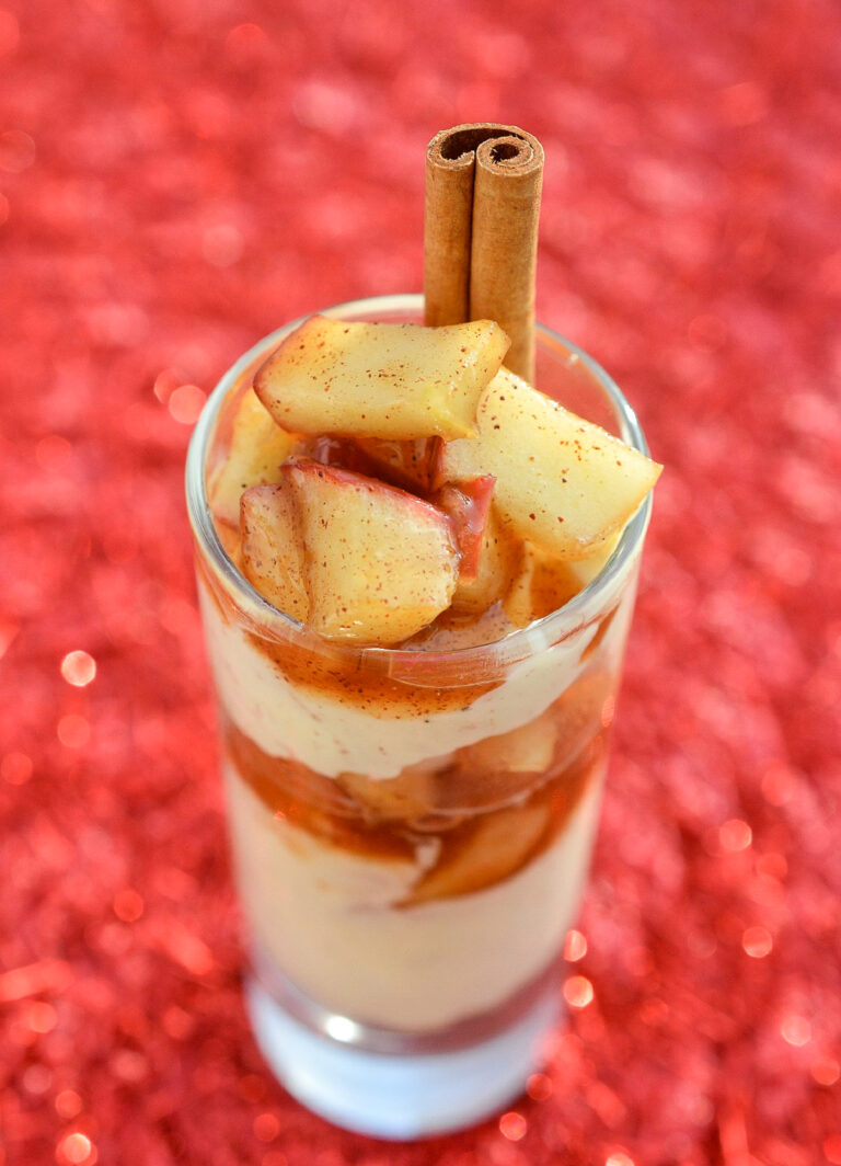 Apple Pie Cheesecake Shooter in a mini dessert glass. Layed no bake cheesecake and fried apples garnished with a cinnamon stick.