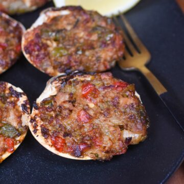 Clams Casino recipe shown cooked on a black plate with a lemon wedge. Stuffed Clams
