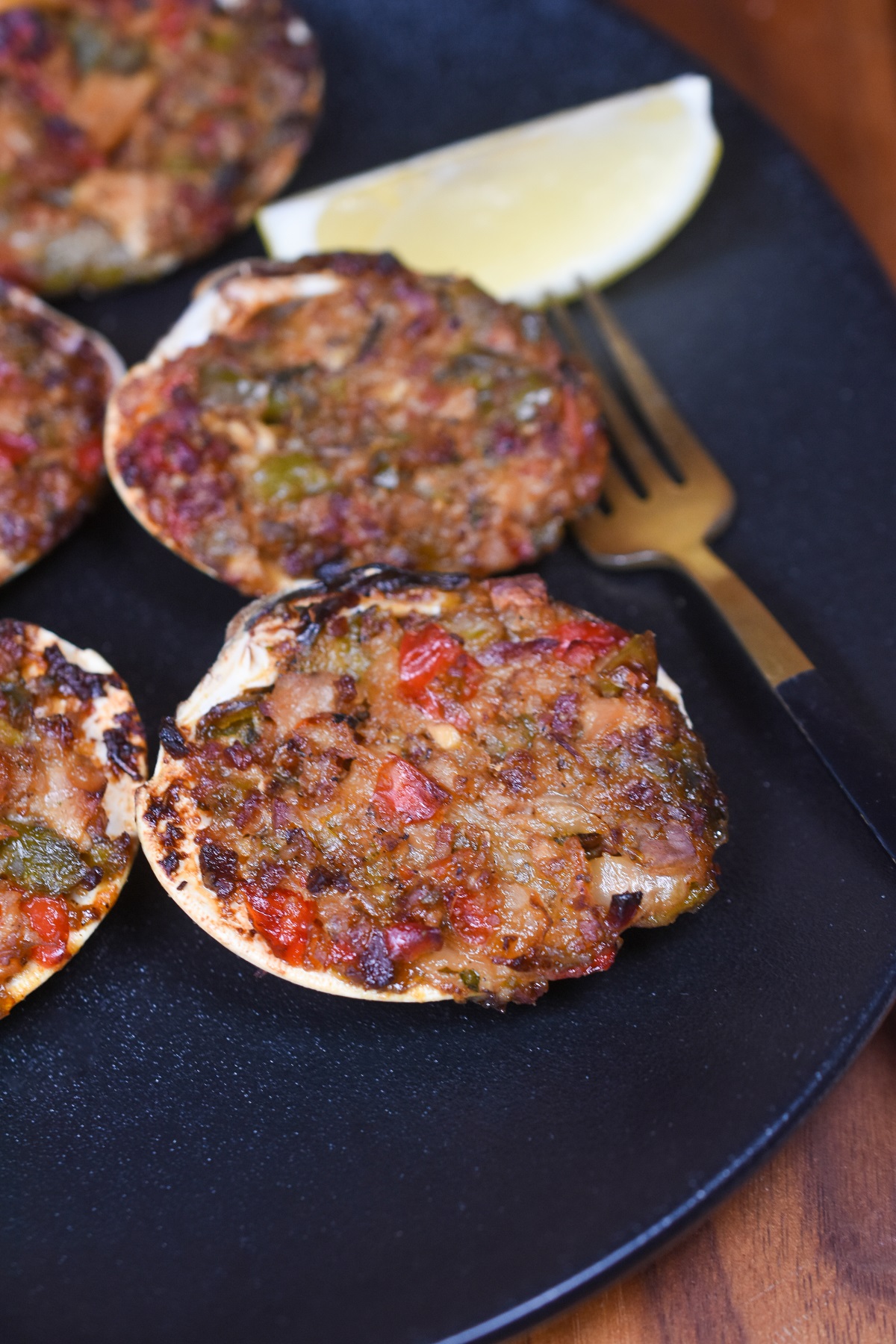 Baked Clams Casino shown on a black plate with lemon wedge and gold fork