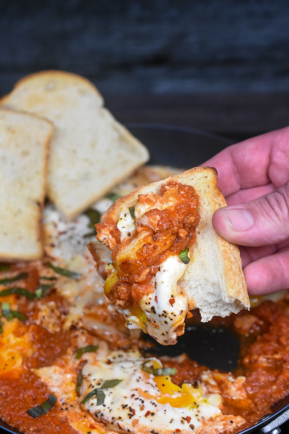 Pan of beans and eggs in tomato sauce being scooped up with a piece of toast. Yolk running.