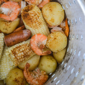 Shrimp Boil recipe, Low Country Boil, Frogmore Stew recipe, shown in a seafood boil pot basket. Shown are corn on cob pieces, potato halves, shrimp in shells and andouille sausage pieces with Creole seasoning