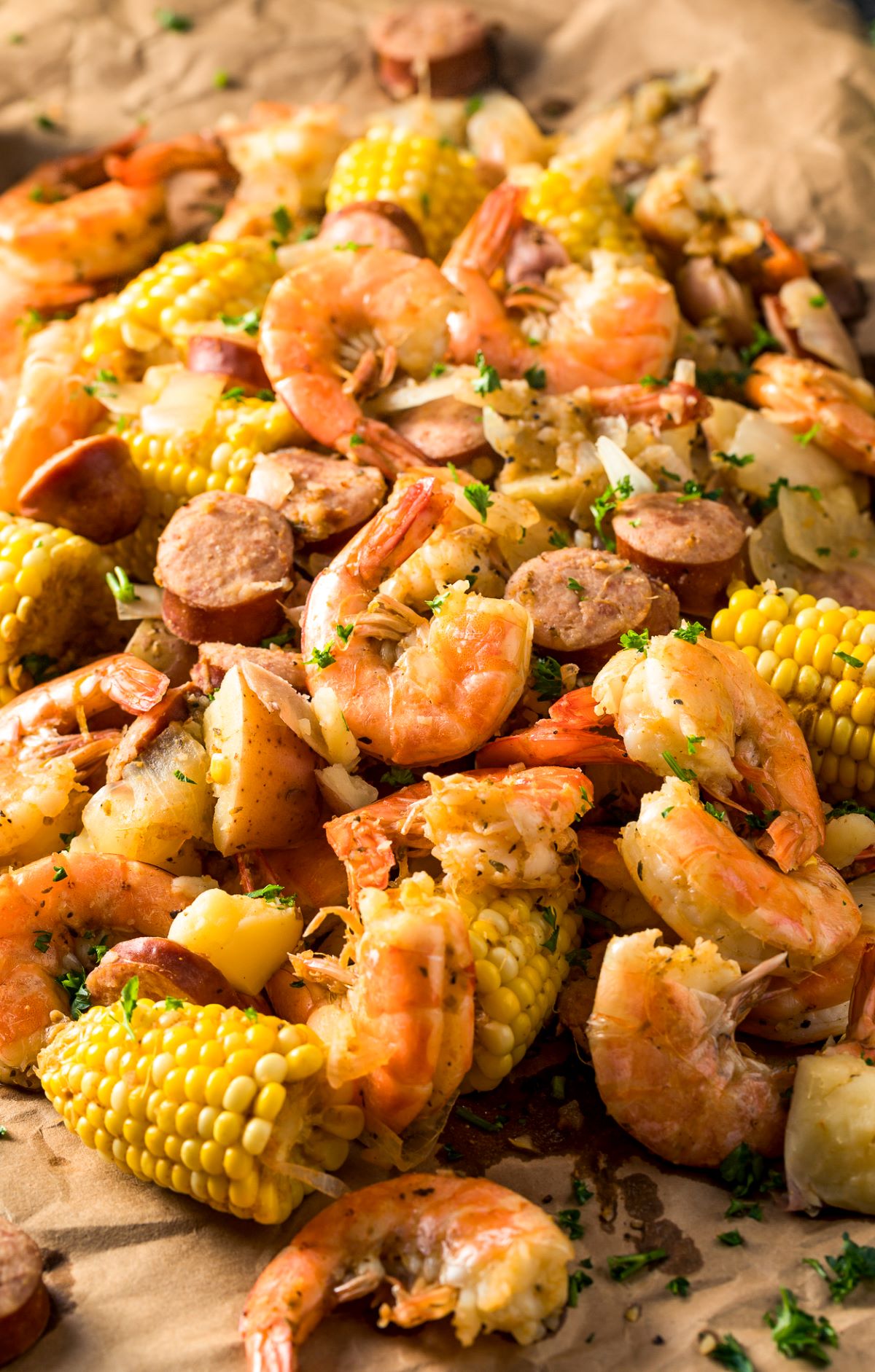 Low Country Boil, Shrimp Boil shown cooked on a platter. A pile of andouille chunks, corn on the cob segments, shrimp in shells and potatoes with creole seasoning. Ready to eat.