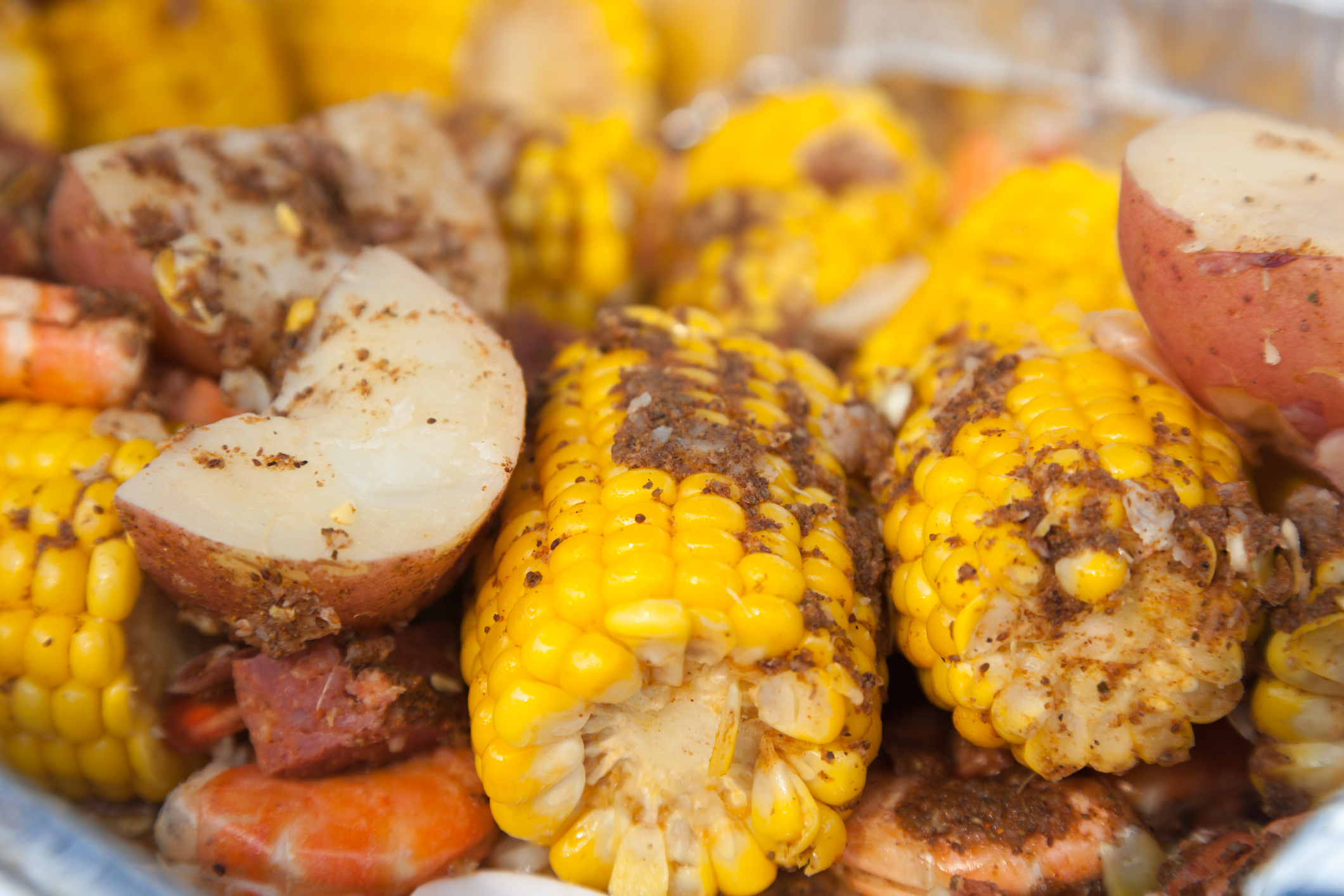 Up close photo of Low Country Boil aka Shrimp Boil, shown on a platter corn on the cob, potato chunks, shrimp in shells and andouille sausage with creole seasoning.