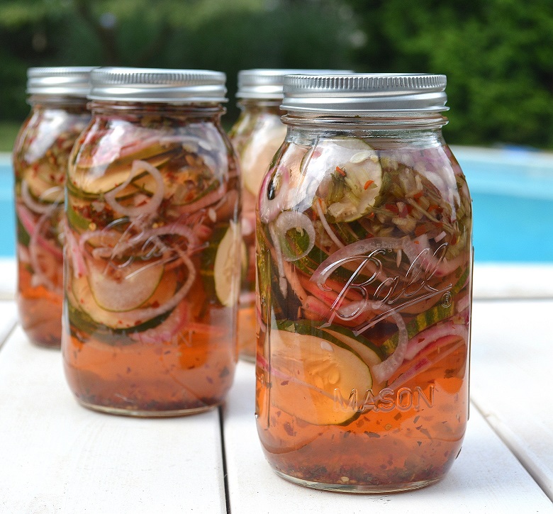 Sweet & Spicy Pickled Cucumbers in a glass jar by a swimming pool