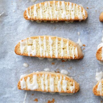 Apple Cider Biscotti recipe shown 6+ biscotti on baking sheet drizzled with apple cider glaze.