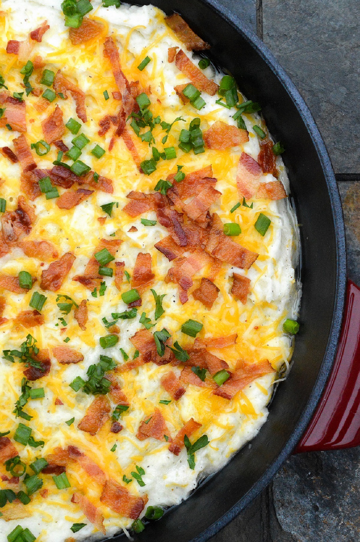 Wondering what to make with leftover mashed potatoes? This Leftover Mashed Potato Recipe is a Loaded Mashed Potato Casserole. Your leftover mashed potatoes repurposed and topped with all the things! Shown in a red and black pan topped with cheese, bacon and chives.