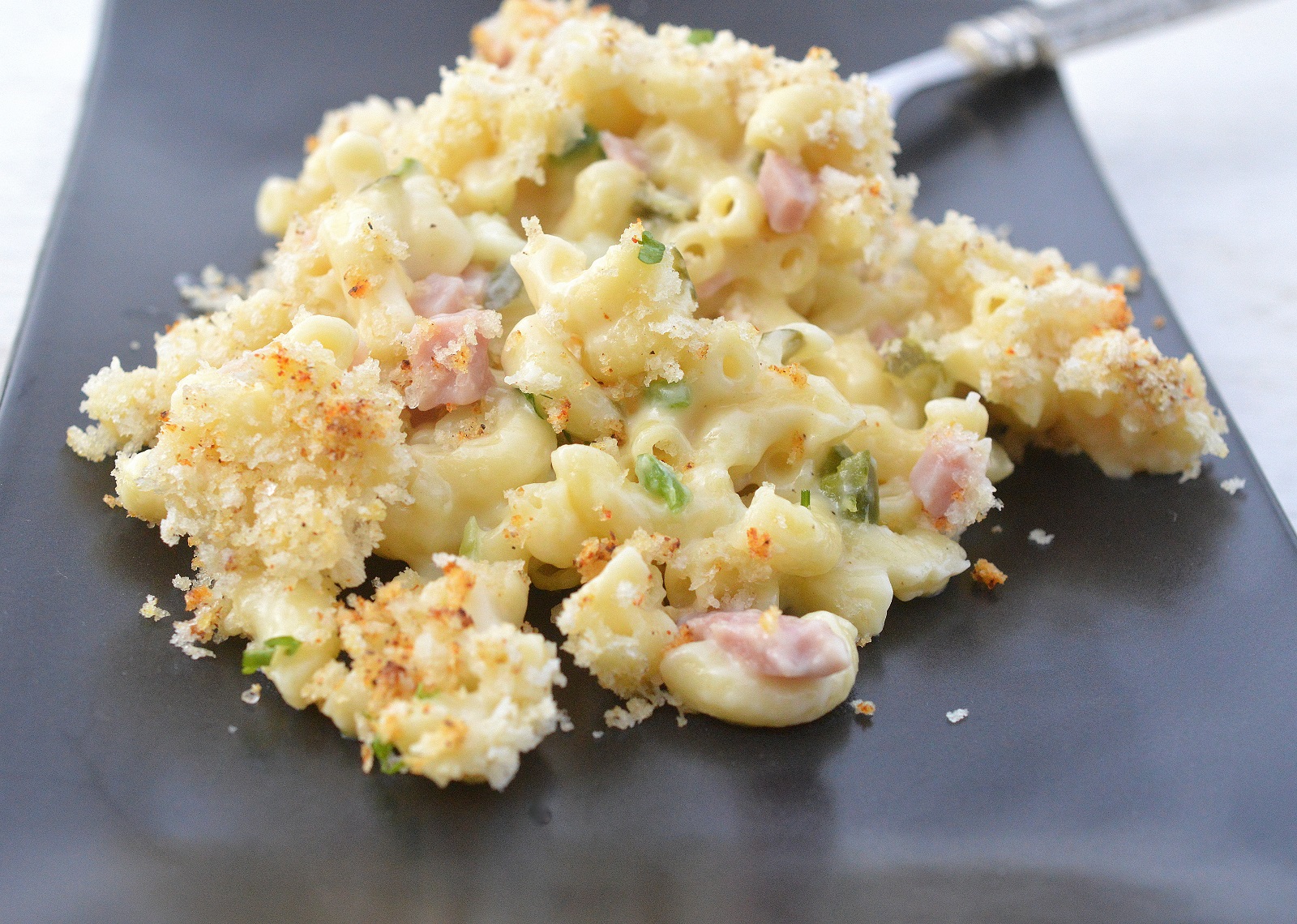 Cuban Sandwich-Style Macaroni & Cheese. Mac and cheese with ham and Panko topping on a black plate 