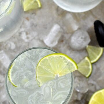 Low Carb Vodka Cooler Drink. Shown glasses fill of ice and lime vodka drink with lime wedge on a metal tray with ice cubes.