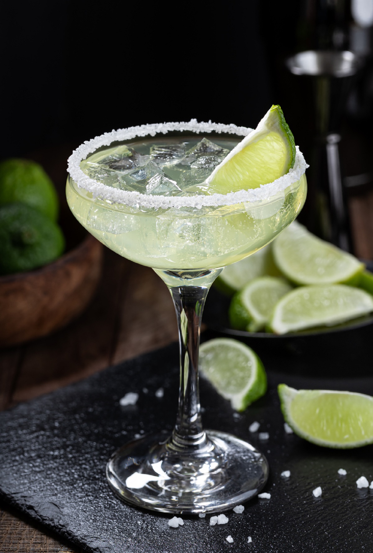 Classic Margaritas by the Pitcher shown in a glass with a salt rim, ice and a lime wedge.
