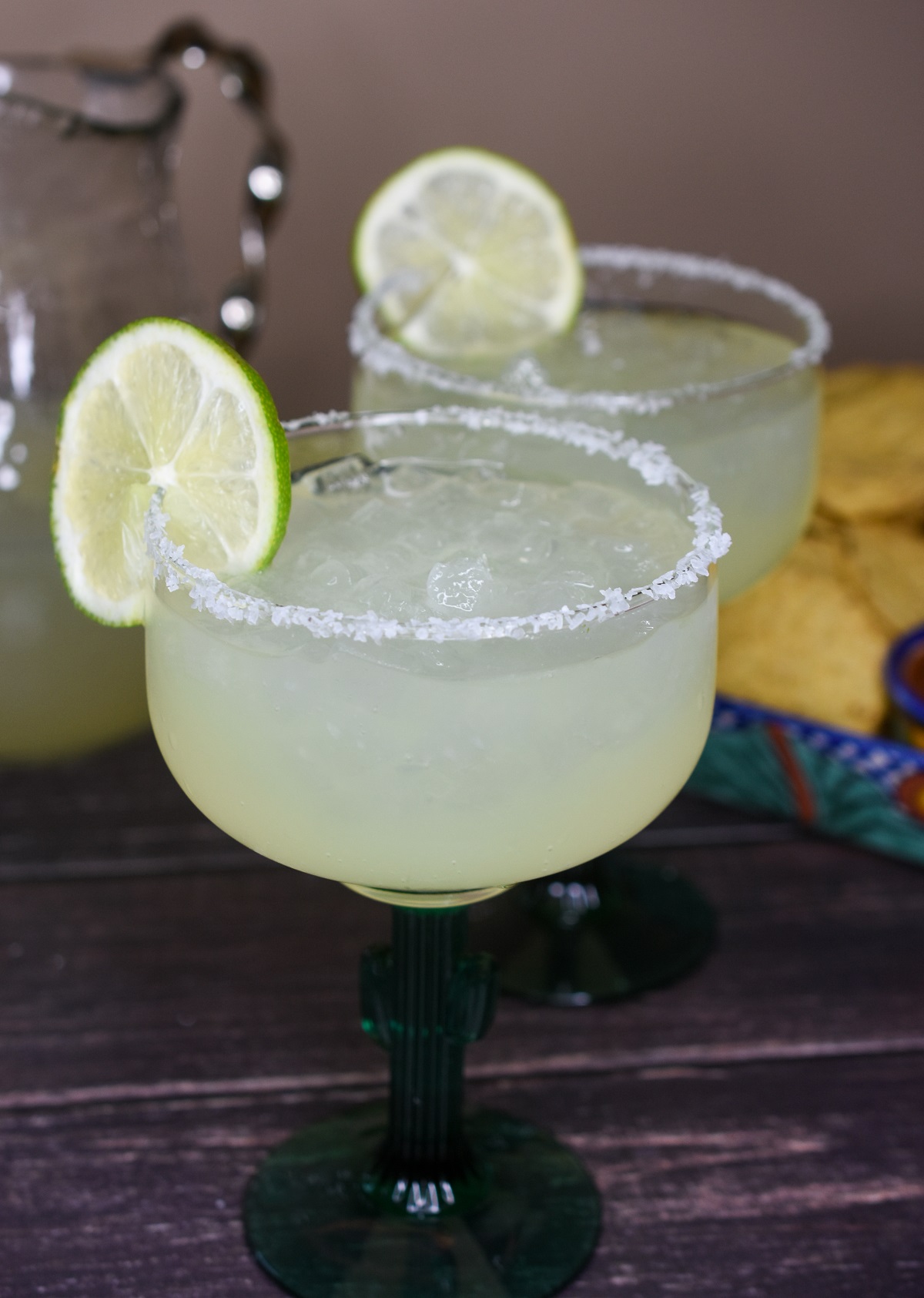 Classic Margaritas recipe. Margaritas by the pitcher. Shown is a cactus margarita glass rimmed with salt with a lime wedge garnish.