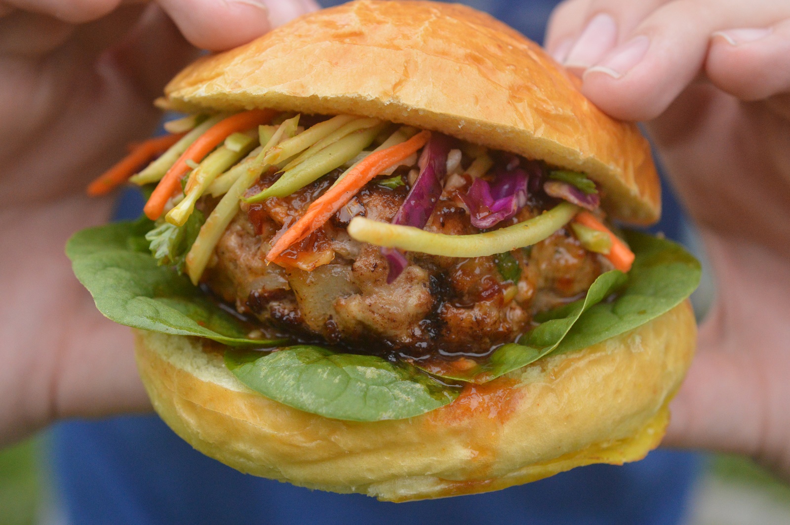 Delicious Asian Pork Burgers with Ginger Honey Glaze. Shown is a pork burger being held with a bun, slaw and Asian glaze.