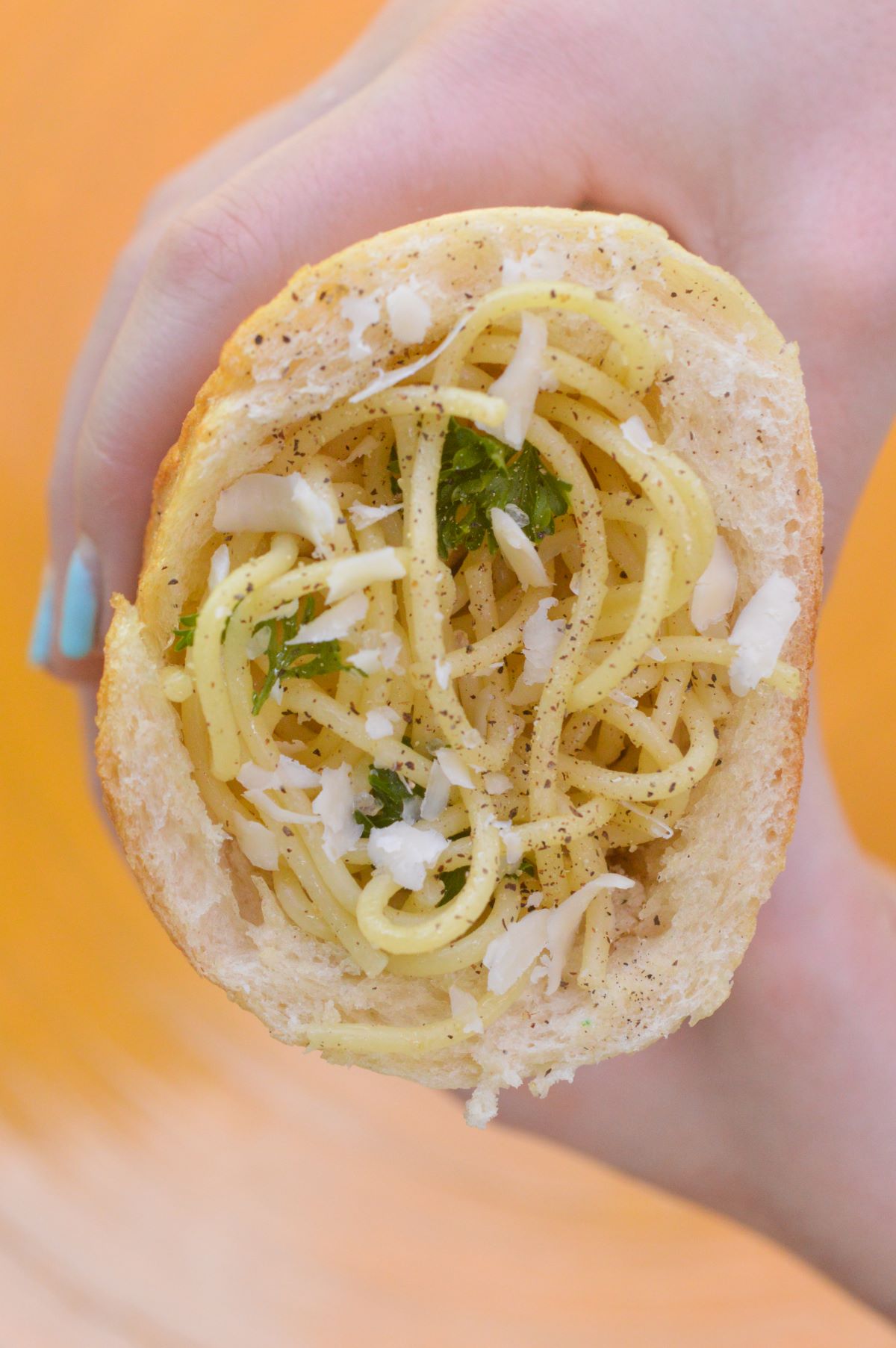 Homemade Pasta Pockets are so fun and delicious to make. Like a homemade hot pocket but better! Shown half piece of French bread hollowed out and stuffed with linguine with garlic sauce, herbs and cheese. held in a hand.