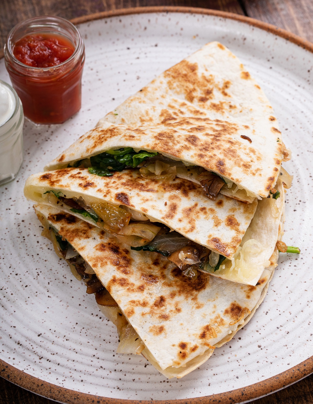 3 Steak Quesadilla quarters shown on a speckled plate with salsa and sour cream in background