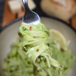 Avocado Pasta made with Avocado Sauce shown green pasta in a bowl with some pasta twirled onto a fork. A roll in the background.