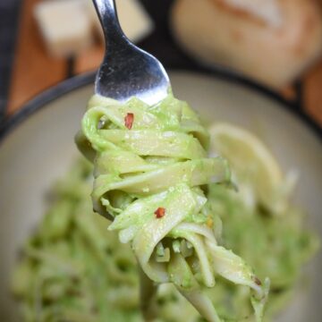 Avocado Pasta made with Avocado Sauce shown green pasta in a bowl with some pasta twirled onto a fork. A roll in the background.
