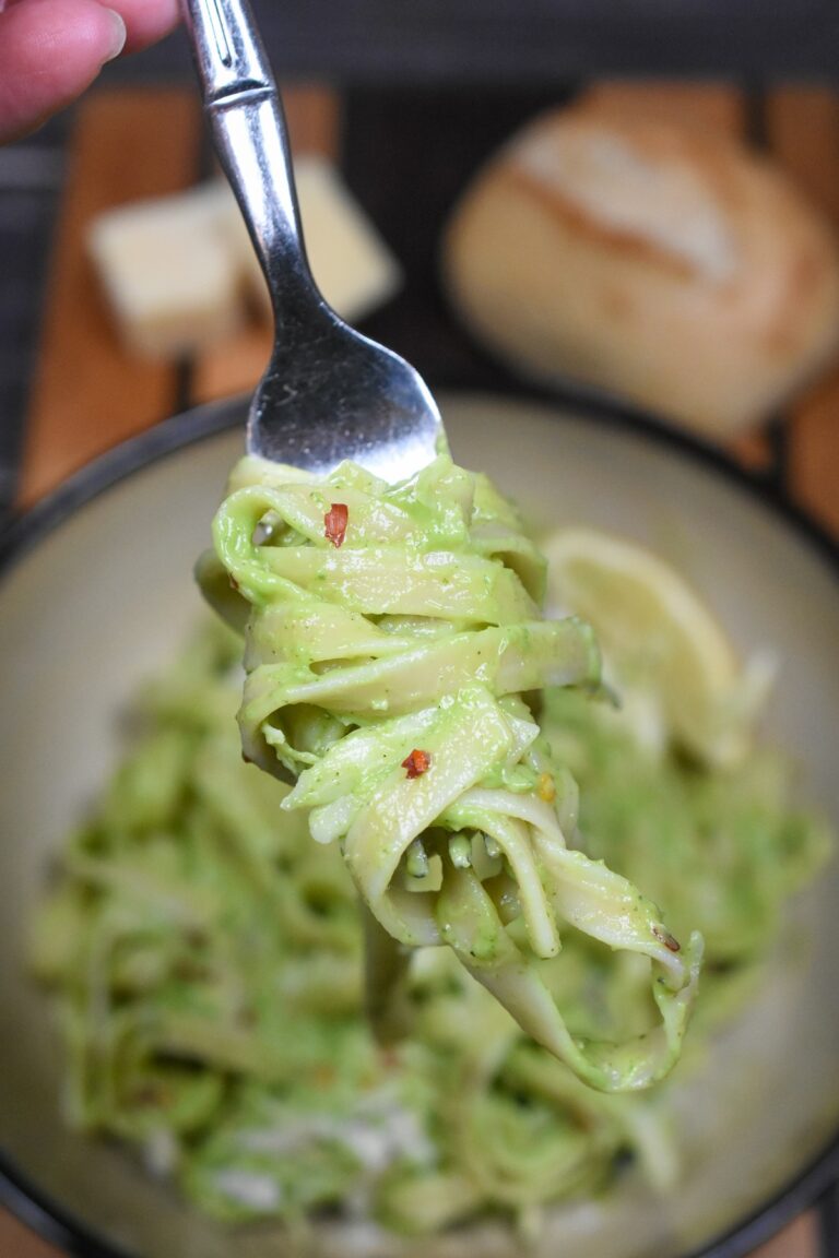 Avocado Pasta made with Avocado Sauce shown green pasta in a bowl with some pasta twirled onto a fork. A roll in the background.
