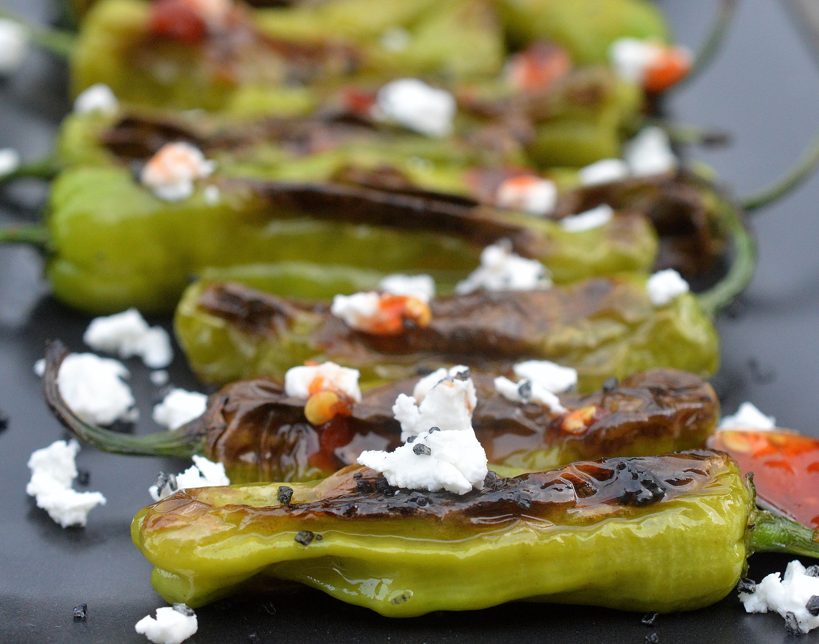 Blistered Shishito Peppers recipe 
topped with goat cheese and spicy honey drizzle