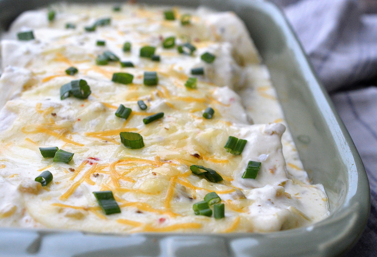 white chicken enchiladas recipe with sour cream sauce in a casserole dish. Chicken and Green Chili Enchiladas