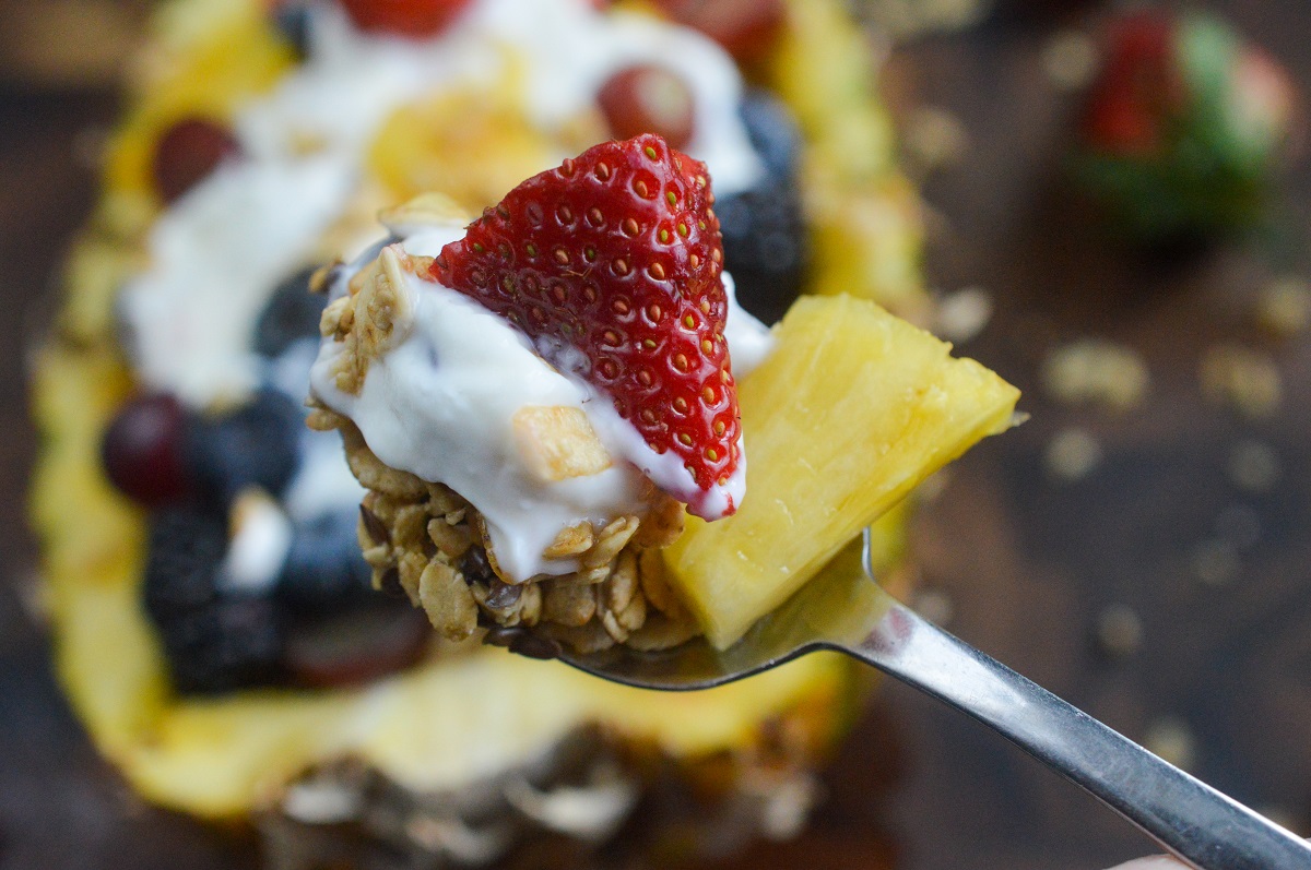 Stuffed Pineapple Yogurt Parfait, this is the best breakfast recipe! It's so delicious! Yogurt, fruit, granola and more in a pineapple bowl. A spoonful of yogurt, granola, pineapple and strawberry on a spoon overtop a stiffed pineapple yogurt bowl