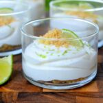 No Bake Key Lime Pie Dessert. shown in clear glass shooter cups. Graham cracker crumbs on bottom, key lime pie filling topped with more crumbs, lime zest and a lime wedge.