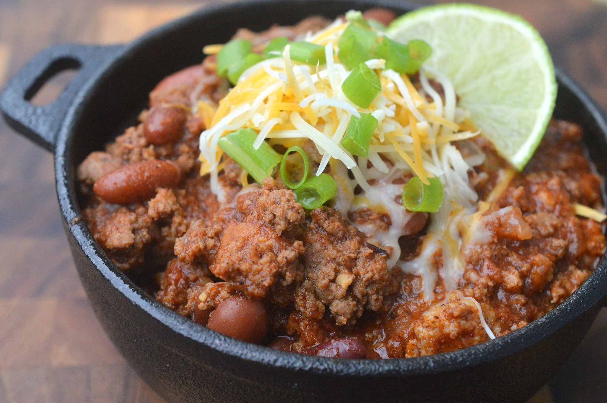 Prize-Winning Beef & Sausage Chili in cast iron bowl topped with cheese and scallions and a lime wedge