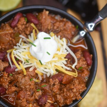 Homemade Chili in bowl with spoon topped with cheese and chives.