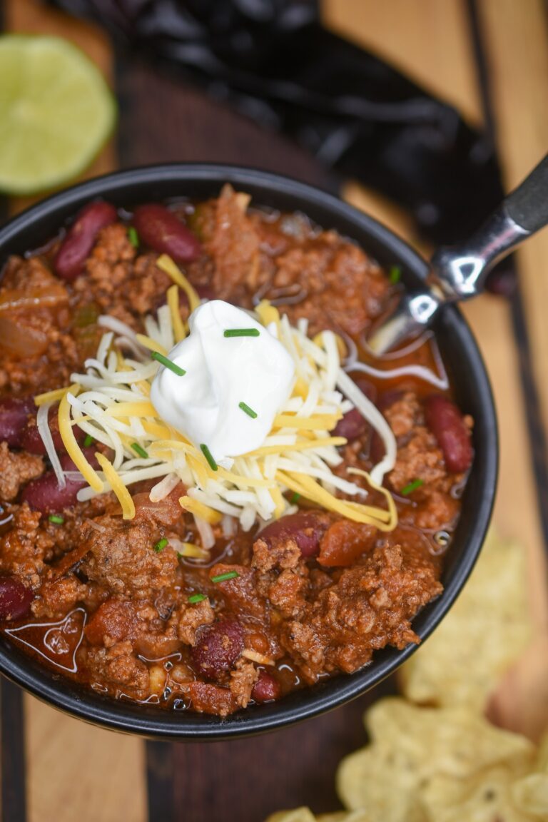Homemade Chili in bowl with spoon topped with cheese and chives.