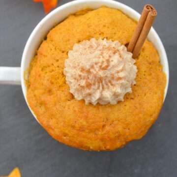 Pumpkin Mug Cake shown in a small ivory mug topped with a dollop of cinnamon icing and a cinnamon stick.