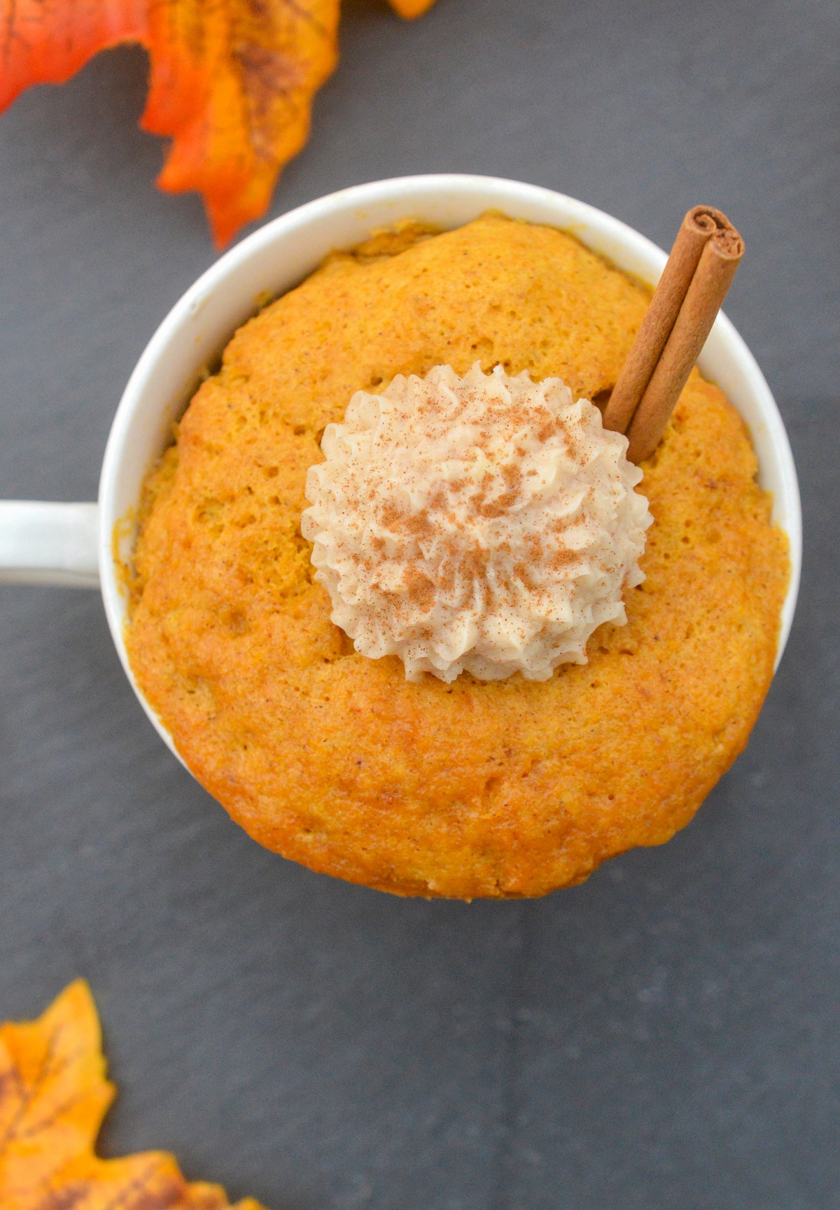 Pumpkin Mug Cake recipe. Shown in an ivory coffee mug topped with a dollop of cinnamon icing and a cinnamon stick.