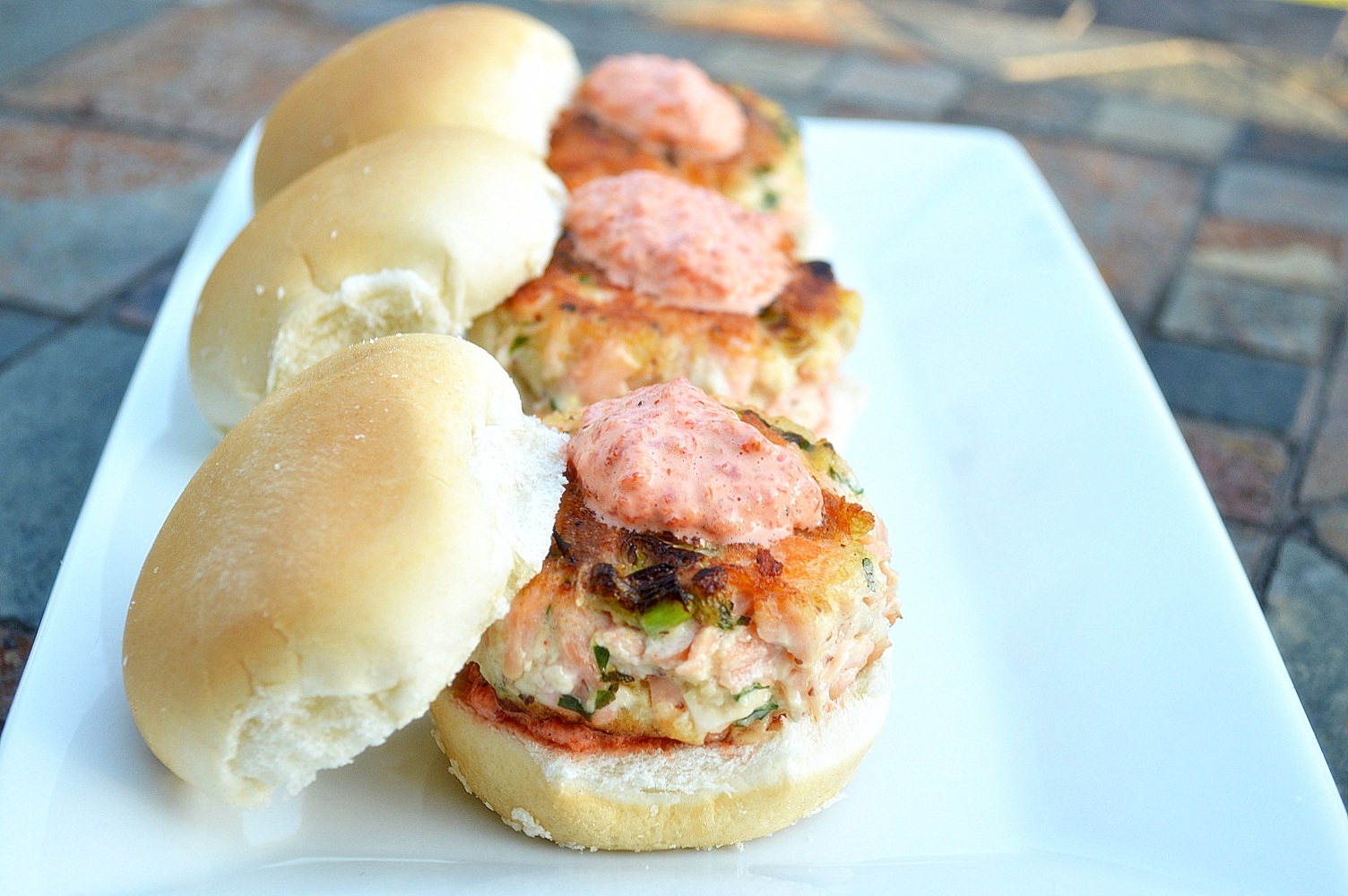 Image of  three salmon sliders on buns on a plate topped with remoulade.